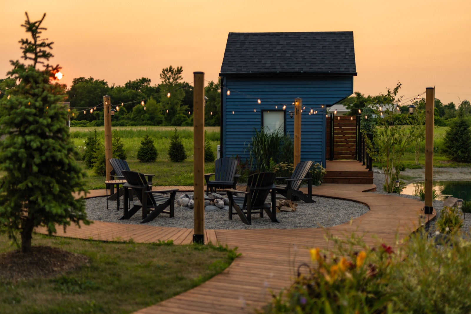 Evening fire pit with Adirondack chairs and string lights overlooking the pond